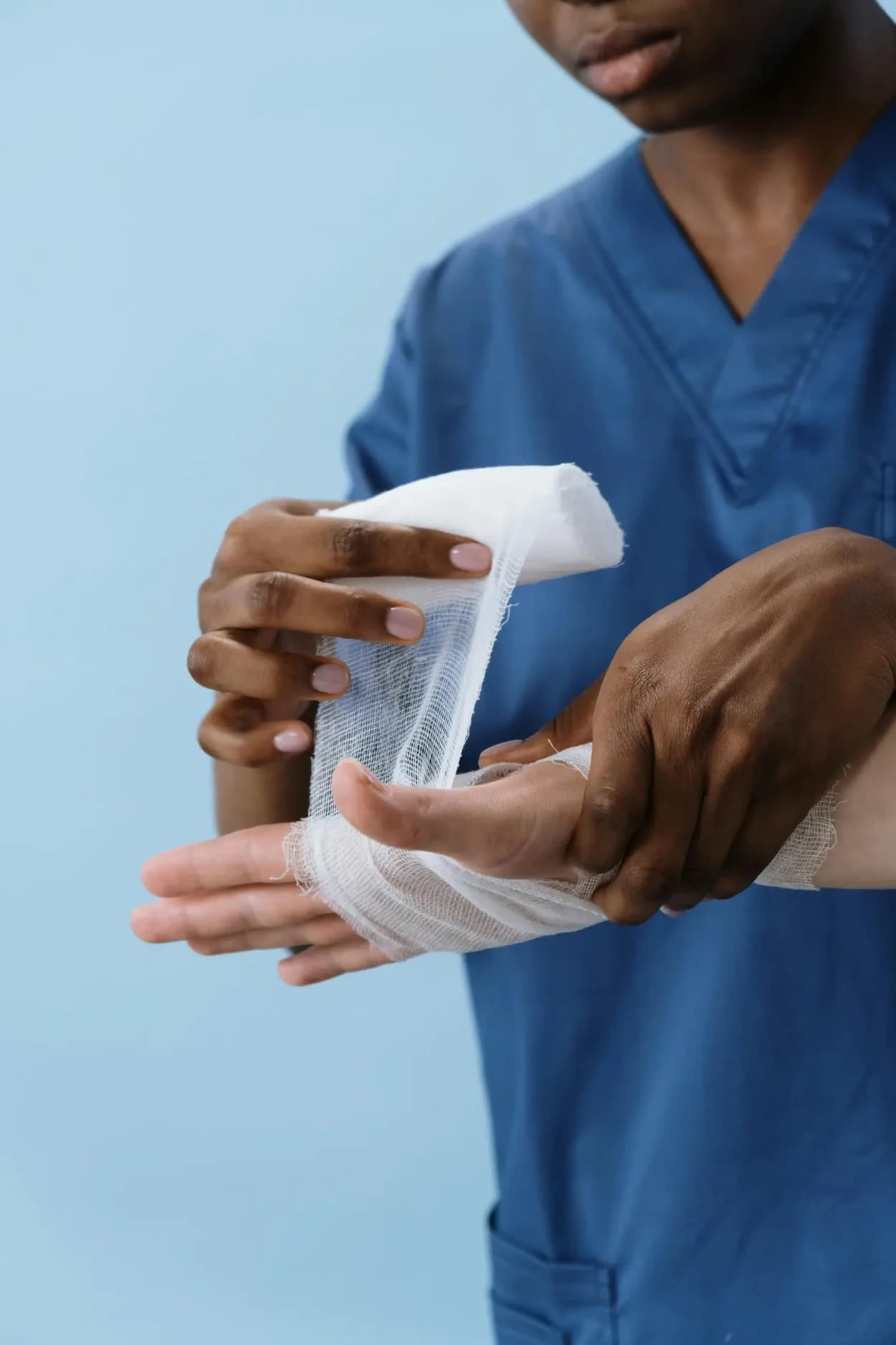 Nurse in scrubs wrapping a bandage around a patient's hand