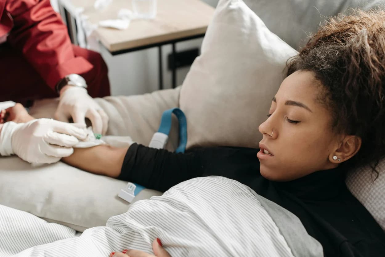 Gloved clinician drawing blood from a patient resting on a couch